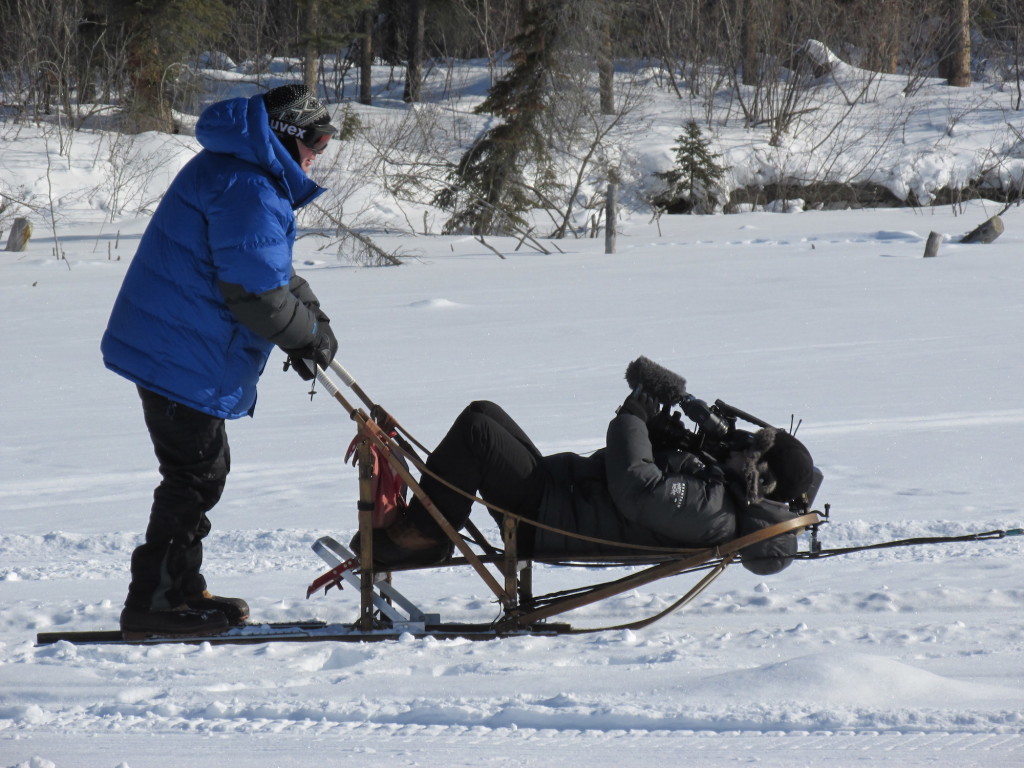 Photographer Andrew Smith films Sean Callebs driving a dog sled. 